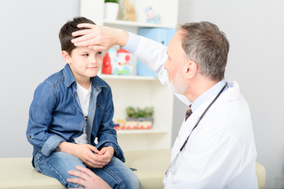 Pediatrician check temperature of his young patient by putting his hand on his forehead