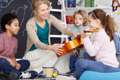 Little preschool girl holding teacher's guitar on music lesson